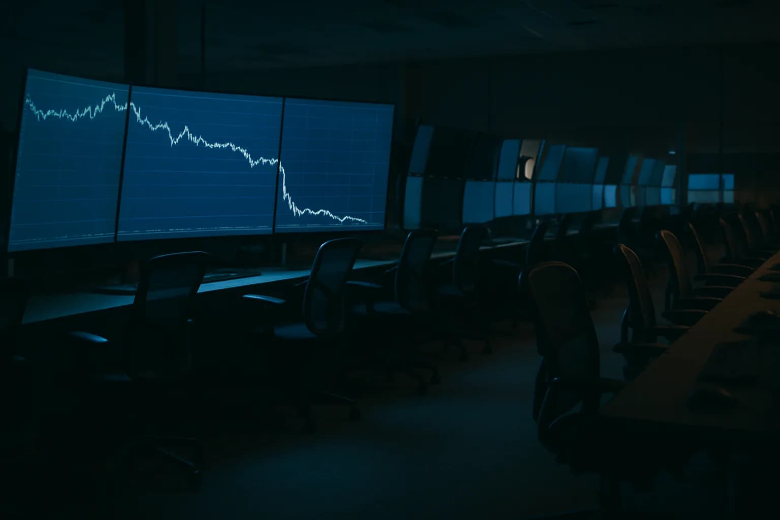 Empty trading floor with crude oil price chart monitors glowing blue in pre-dawn light, chairs vacant before the session opens