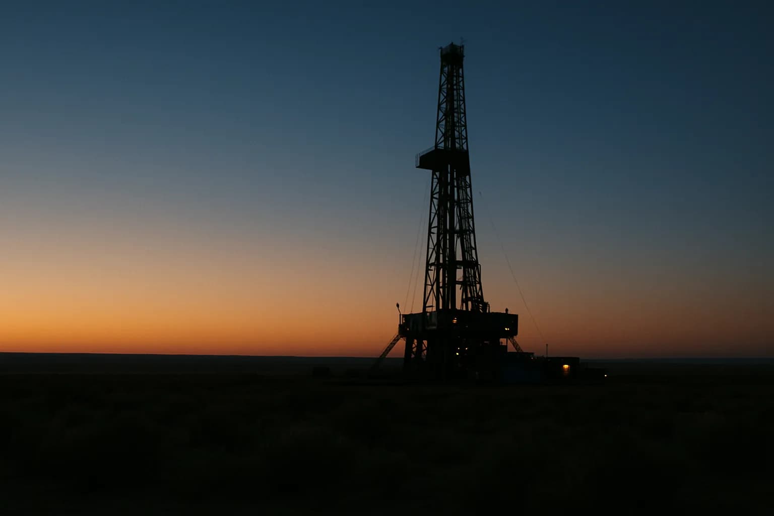 A drilling rig silhouetted against an orange and blue dusk sky in a Utah desert landscape, surrounded by sage scrubland.