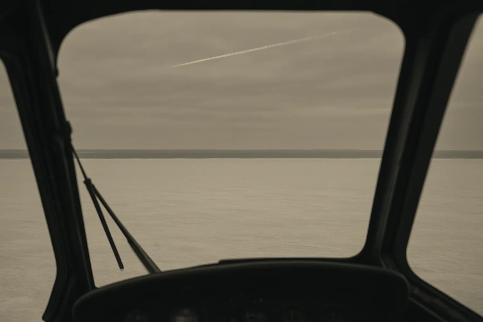 Aerial view of a frozen gray lake under overcast winter sky, a dissipating contrail crossing the upper frame
